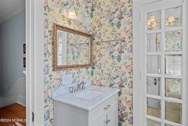 bathroom with crown molding, vanity, and wallpapered walls