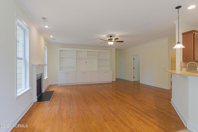 unfurnished living room featuring plenty of natural light, ceiling fan, crown molding, and light wood-type flooring