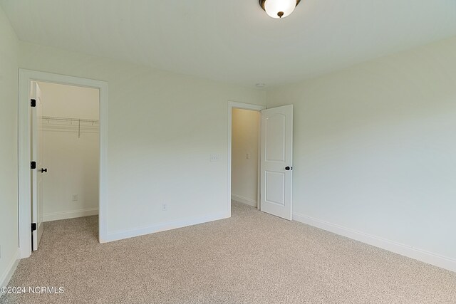 unfurnished bedroom featuring a spacious closet, a closet, and light carpet