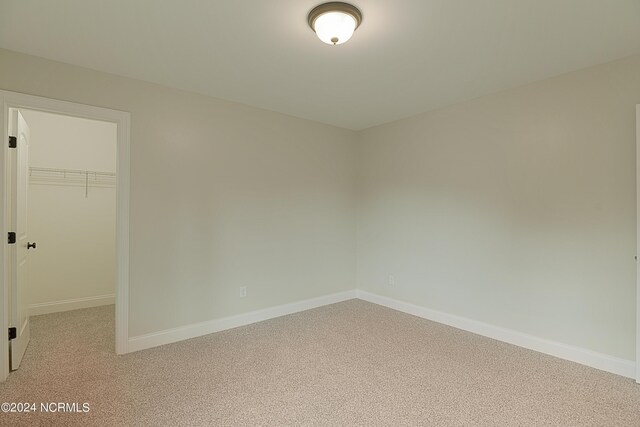 unfurnished bedroom featuring a walk in closet, light colored carpet, and a closet