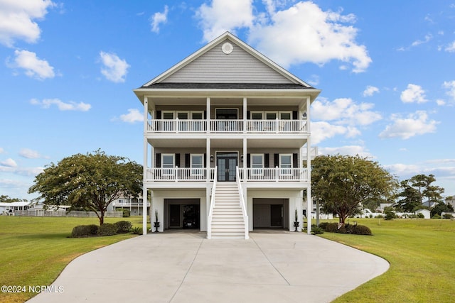 coastal inspired home with an attached garage, a balcony, stairs, driveway, and a front yard