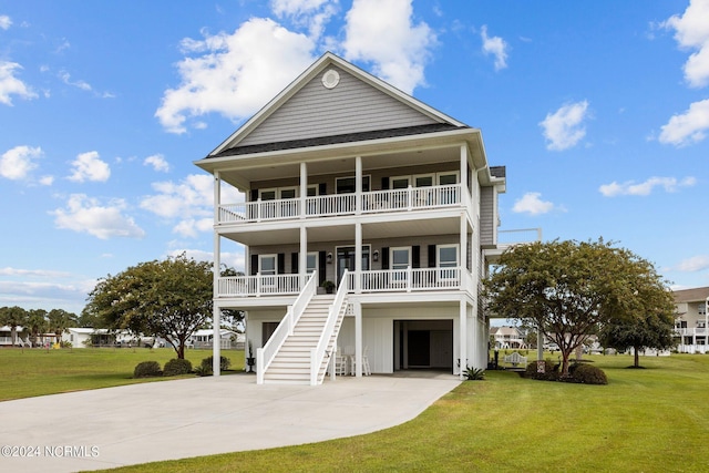 beach home with a balcony, covered porch, concrete driveway, stairway, and a front yard