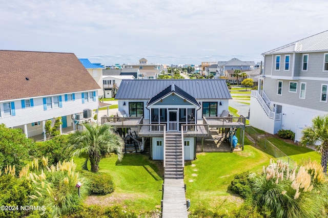 rear view of property with a sunroom, a standing seam roof, a lawn, and stairs