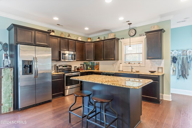 kitchen with pendant lighting, a kitchen island, appliances with stainless steel finishes, crown molding, and dark hardwood / wood-style flooring