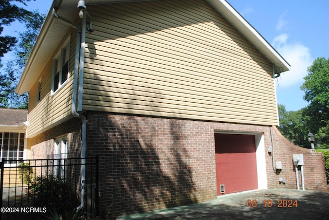 view of property exterior with a garage, brick siding, fence, and aphalt driveway