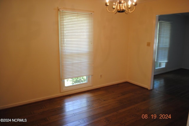 spare room with a chandelier, dark wood finished floors, and baseboards