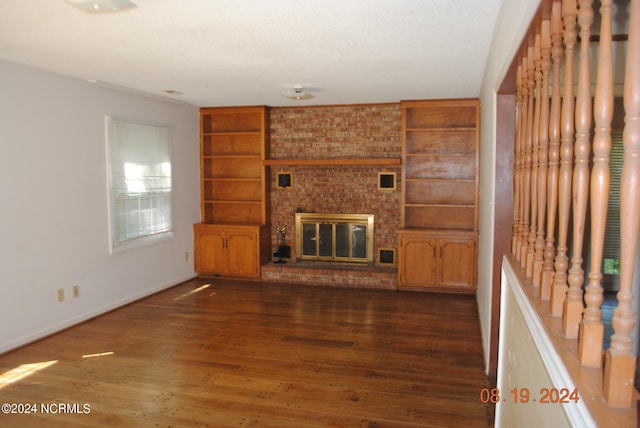 unfurnished living room with a fireplace, brick wall, dark wood-type flooring, and built in shelves