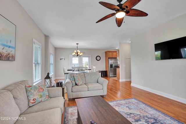 living area with light wood-style flooring, baseboards, and ceiling fan with notable chandelier