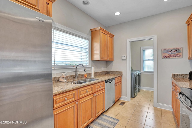 kitchen with appliances with stainless steel finishes, light stone counters, independent washer and dryer, a sink, and light tile patterned flooring