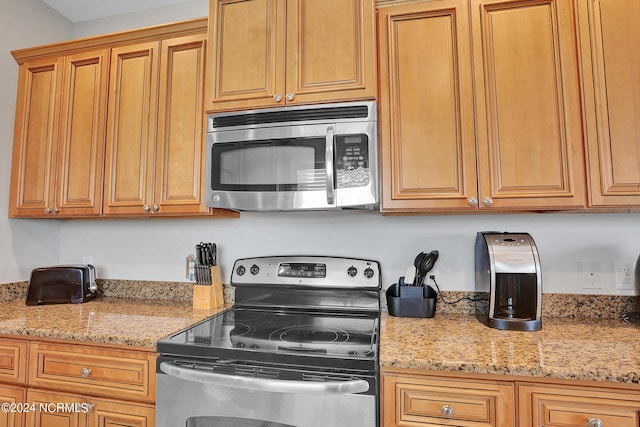 kitchen featuring stainless steel appliances, brown cabinets, and light stone counters