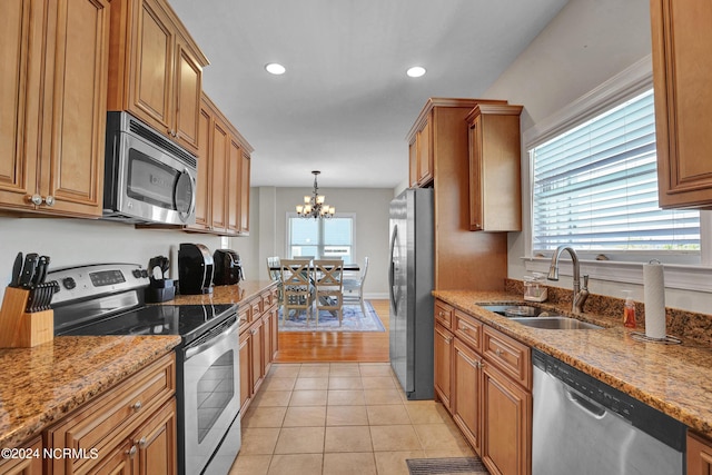 kitchen with appliances with stainless steel finishes, brown cabinetry, a sink, and light stone countertops