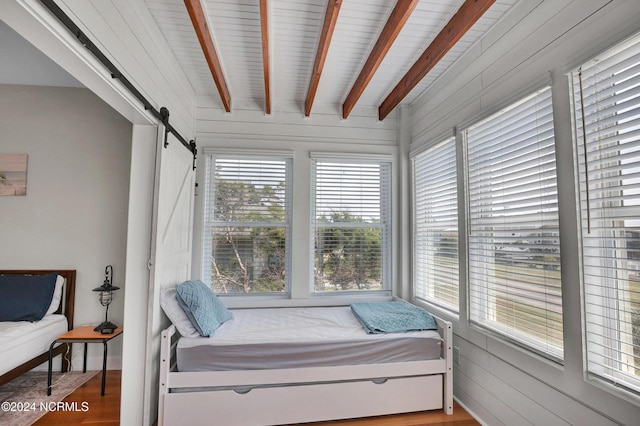 bedroom featuring a barn door, beam ceiling, and wood finished floors