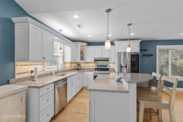 kitchen with appliances with stainless steel finishes, light hardwood / wood-style floors, decorative backsplash, sink, and pendant lighting