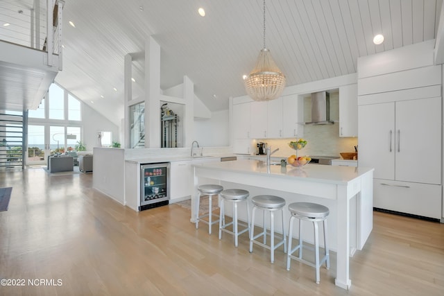 kitchen featuring backsplash, beverage cooler, light countertops, white cabinetry, and wall chimney exhaust hood
