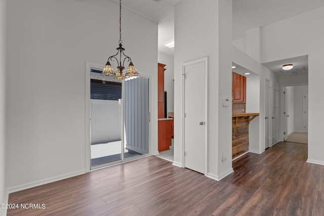 unfurnished dining area with a high ceiling, an inviting chandelier, and dark hardwood / wood-style flooring