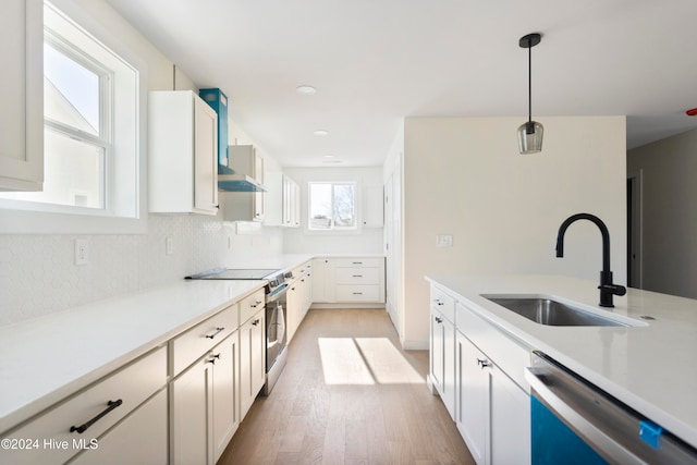 kitchen with sink, appliances with stainless steel finishes, hanging light fixtures, light hardwood / wood-style flooring, and wall chimney range hood