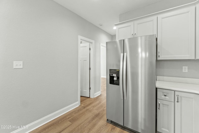 kitchen with stainless steel fridge, white cabinets, and light wood-type flooring