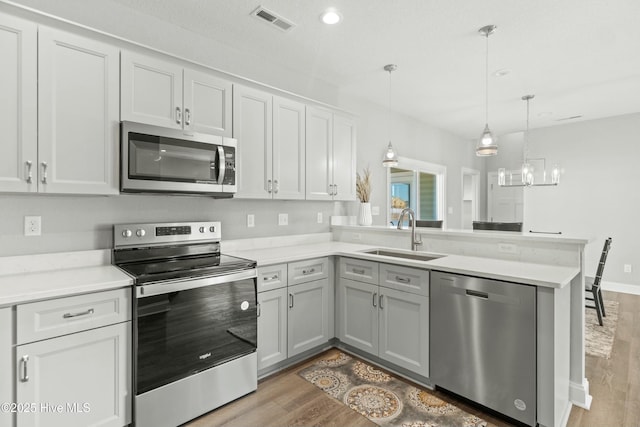 kitchen featuring decorative light fixtures, sink, light hardwood / wood-style floors, kitchen peninsula, and stainless steel appliances