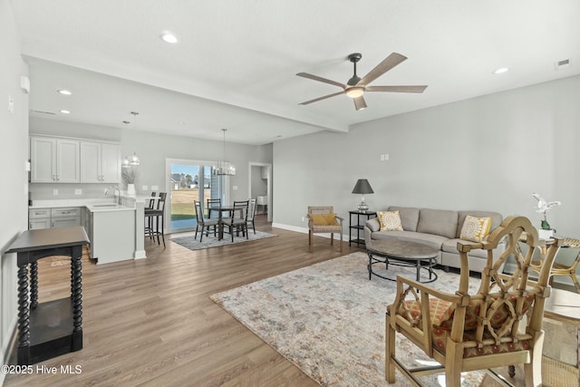 living room featuring beamed ceiling, sink, ceiling fan with notable chandelier, and light wood-type flooring