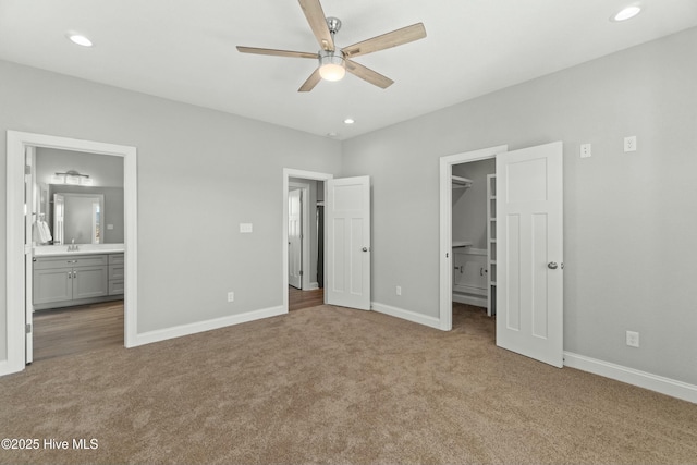 unfurnished bedroom featuring ensuite bathroom, a walk in closet, light carpet, a closet, and ceiling fan