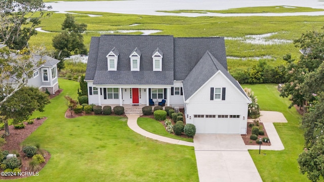 cape cod house featuring covered porch, a water view, a front yard, a garage, and driveway