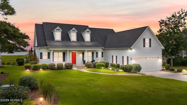 cape cod-style house with covered porch, a lawn, and a garage