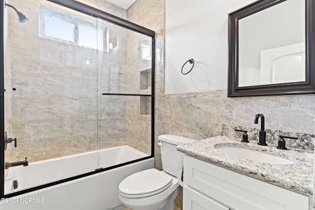 full bathroom featuring tile walls, shower / bath combination with glass door, vanity, and toilet