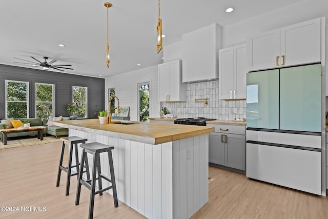 kitchen with white cabinetry, sink, refrigerator, pendant lighting, and an island with sink