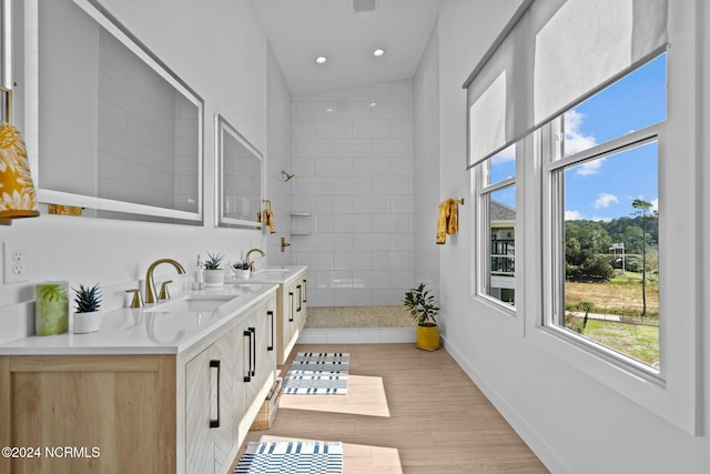 bathroom featuring hardwood / wood-style flooring, vanity, a tile shower, and vaulted ceiling