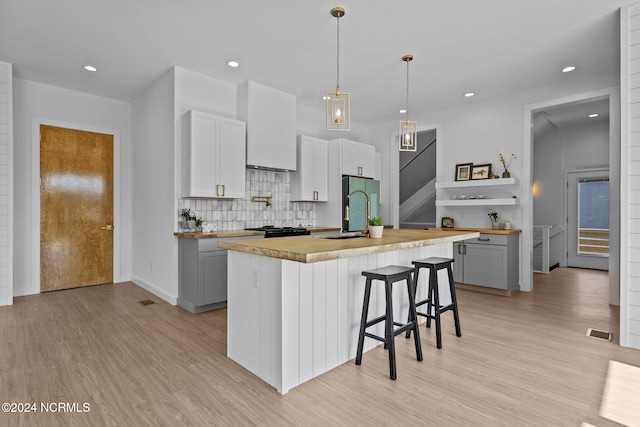 kitchen with sink, an island with sink, pendant lighting, gray cabinets, and light wood-type flooring