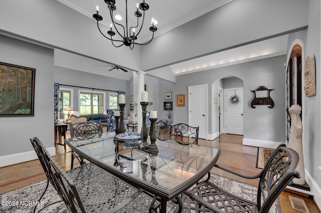 dining area featuring arched walkways, decorative columns, a towering ceiling, wood finished floors, and baseboards