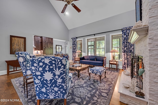 living area with a fireplace, ceiling fan, wood finished floors, high vaulted ceiling, and baseboards