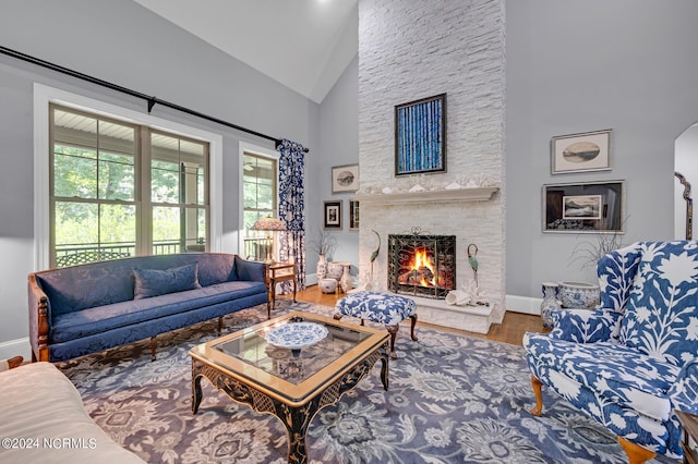 living area featuring high vaulted ceiling, a stone fireplace, baseboards, and wood finished floors