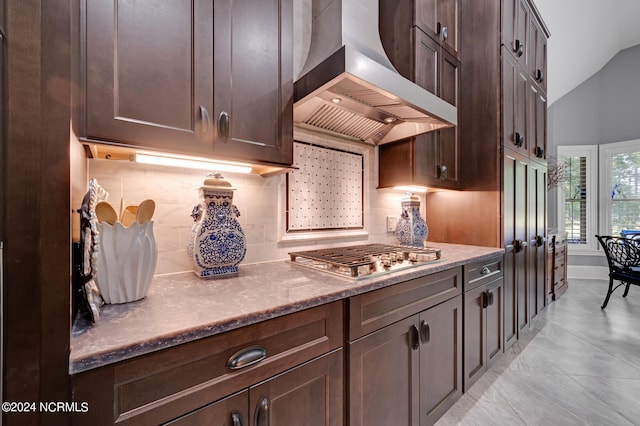 kitchen with lofted ceiling, stainless steel gas cooktop, dark brown cabinets, decorative backsplash, and wall chimney exhaust hood