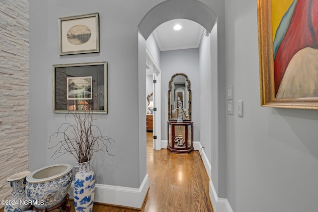 corridor with arched walkways, crown molding, baseboards, and wood finished floors