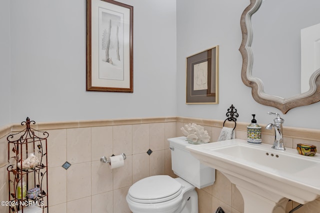 half bath featuring wainscoting, a sink, tile walls, and toilet