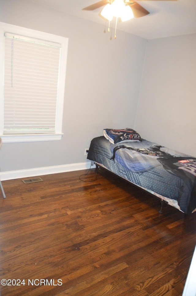 bedroom with a ceiling fan, visible vents, baseboards, and wood finished floors