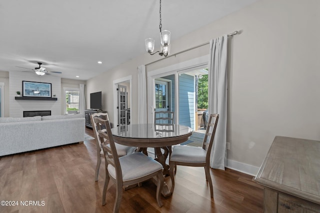 dining space featuring ceiling fan with notable chandelier, dark wood-type flooring, and a fireplace