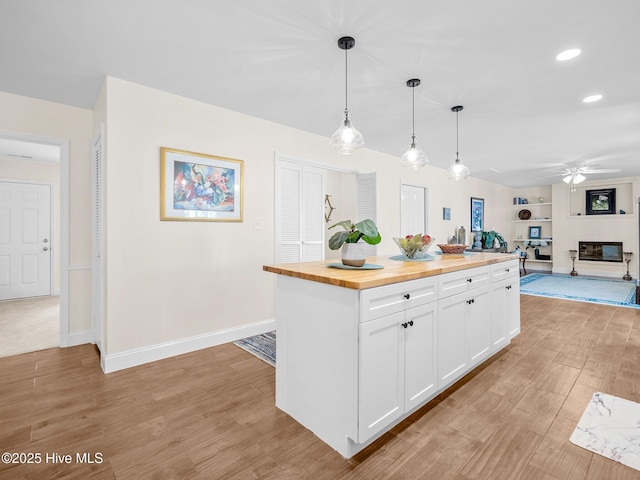 kitchen with butcher block countertops, a ceiling fan, built in features, white cabinetry, and light wood-style floors