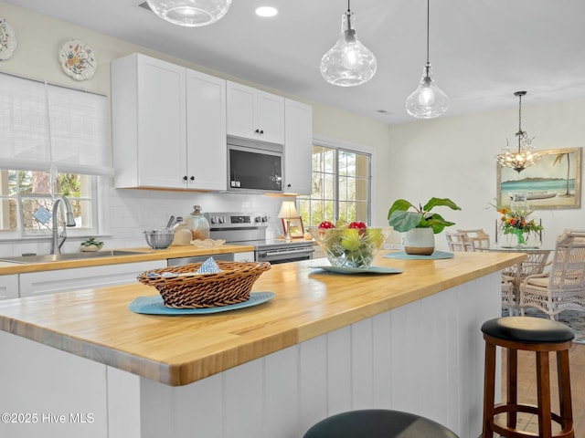 kitchen with butcher block counters, a wealth of natural light, stainless steel appliances, white cabinetry, and a sink