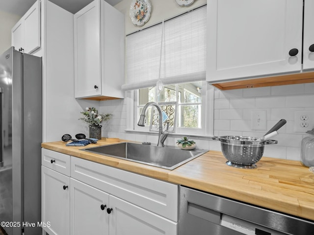 kitchen featuring dishwashing machine, freestanding refrigerator, a sink, butcher block countertops, and white cabinets