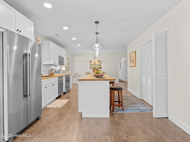 kitchen with light wood-style flooring, butcher block countertops, stainless steel appliances, white cabinets, and a kitchen breakfast bar