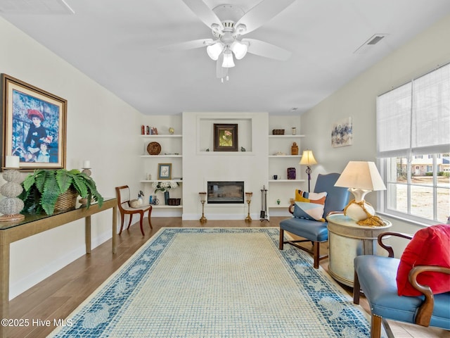 interior space featuring a glass covered fireplace, wood finished floors, visible vents, and a ceiling fan