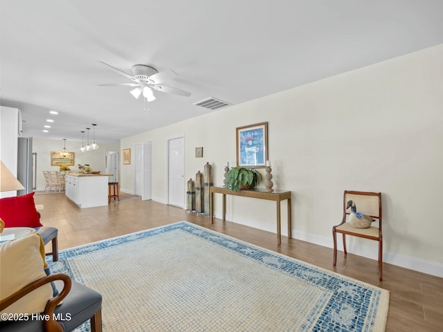 sitting room featuring light wood-style flooring, a ceiling fan, visible vents, and baseboards