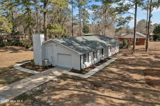 view of side of home featuring central AC unit, driveway, an attached garage, stucco siding, and a shingled roof