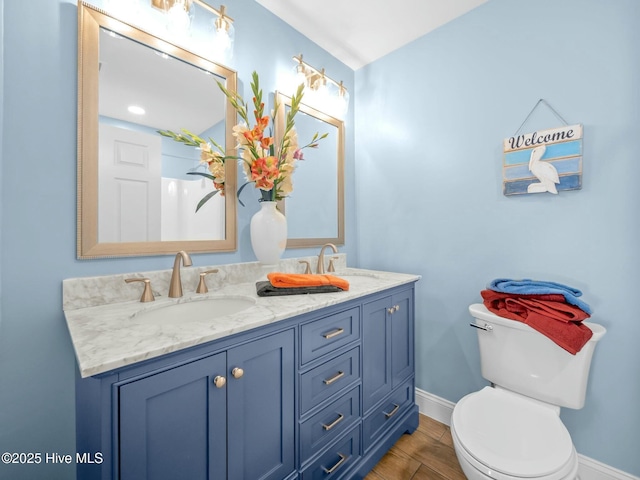 bathroom with a sink, baseboards, toilet, and double vanity