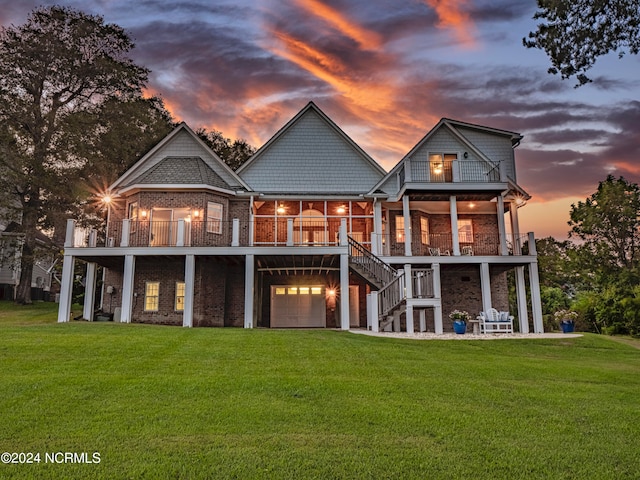 back house at dusk featuring a balcony and a yard