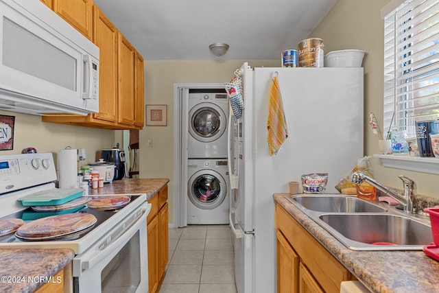 kitchen featuring white appliances, light tile patterned floors, stacked washer and clothes dryer, brown cabinets, and a sink