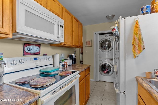 kitchen with light tile patterned floors, stacked washer and dryer, white appliances, and brown cabinets