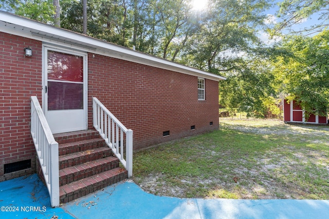 view of side of home featuring entry steps, a lawn, an outbuilding, crawl space, and brick siding